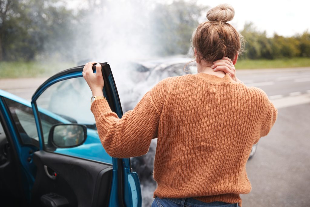 Una mujer saliendo de su carro después de chocar con la mano en el cuello mostrando señales de dolor.